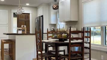 A modern kitchen with white cabinets, a wooden dining table, and a chandelier.