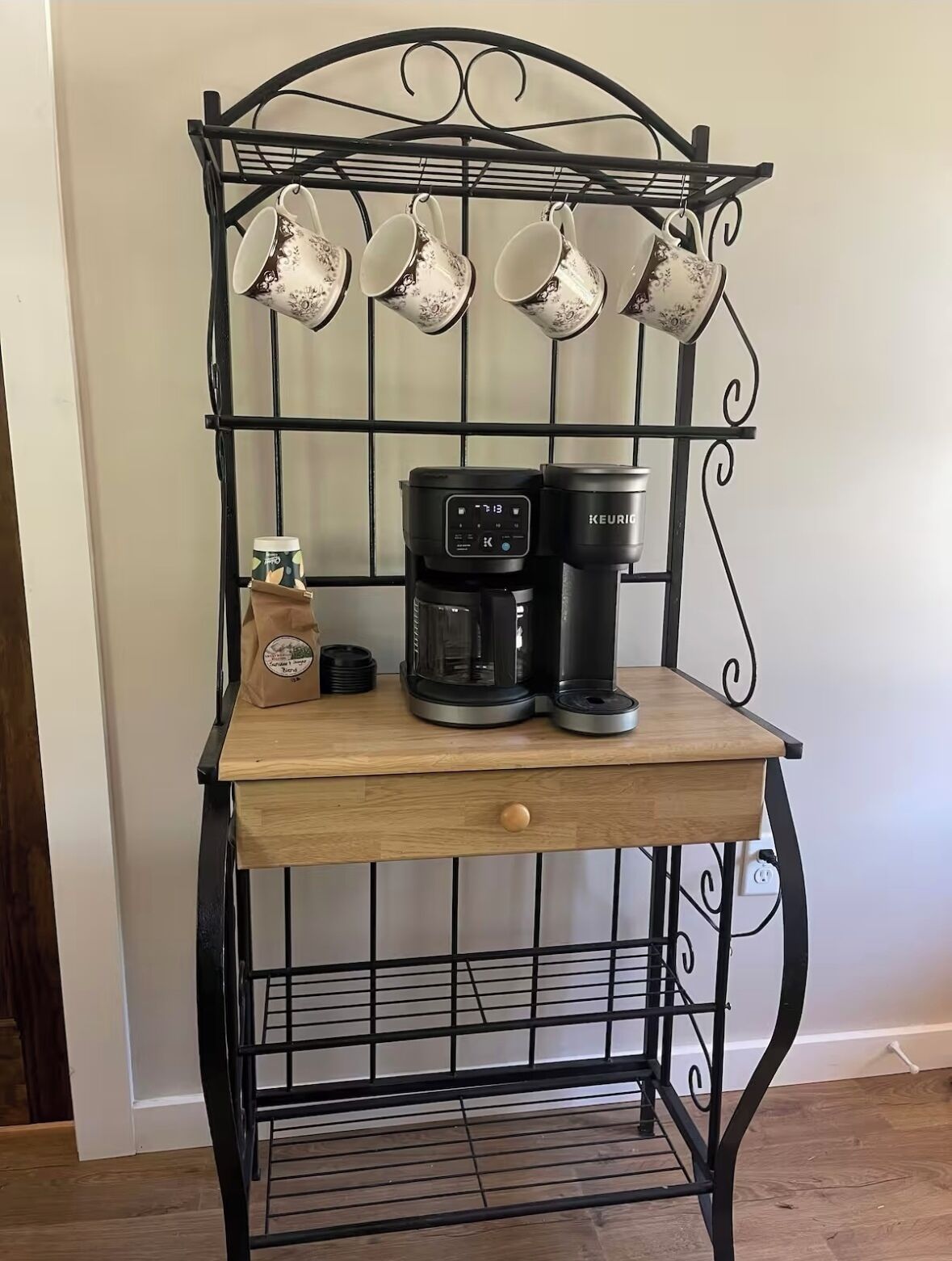 Un présentoir à café en métal, comprenant une machine à café et des tasses, un sac en papier brun et une petite table en bois.
