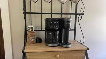 Un présentoir à café en métal, comprenant une machine à café et des tasses, un sac en papier brun et une petite table en bois.