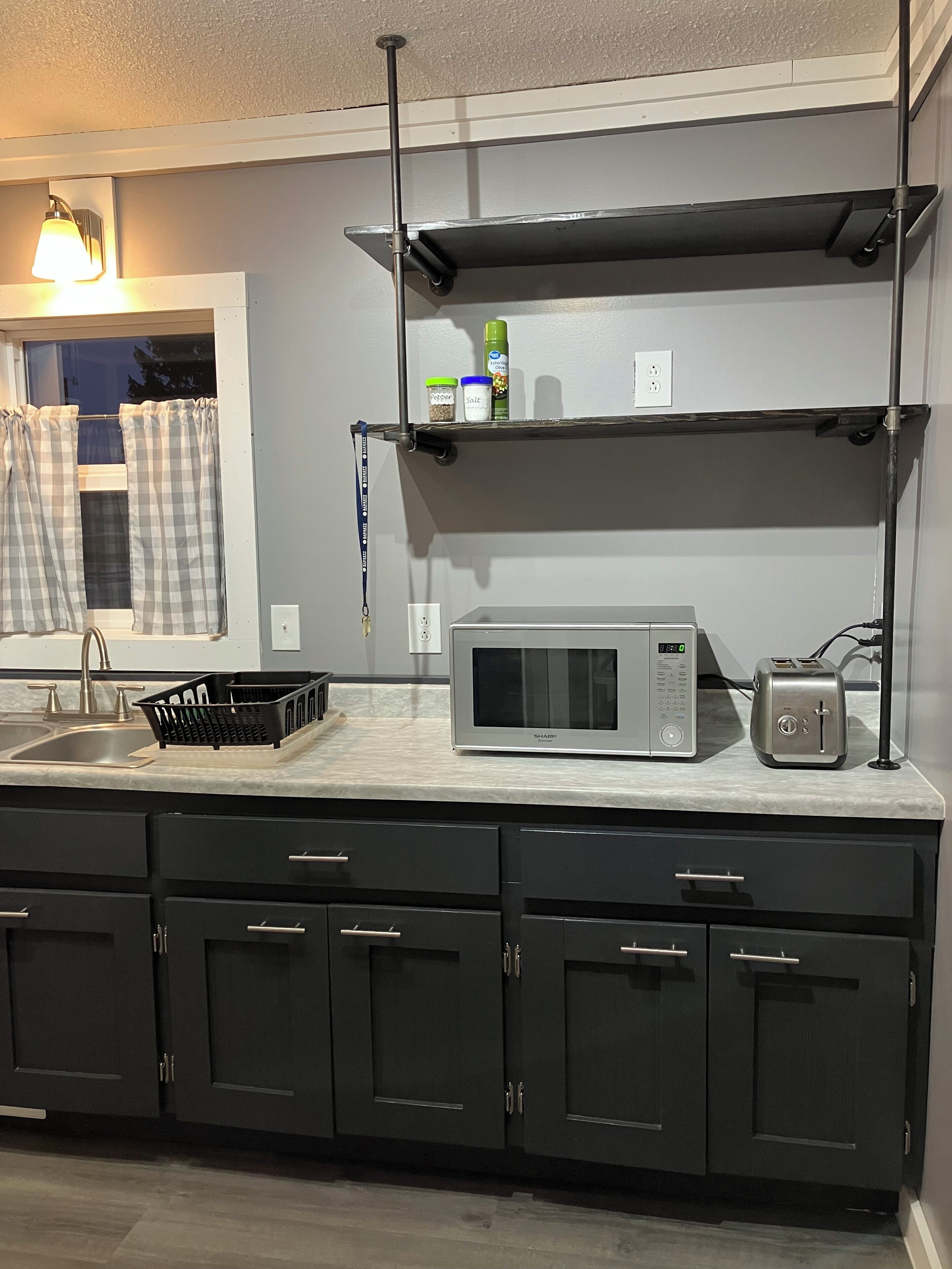 A kitchen with a microwave, toaster, and shelves with kitchen items.