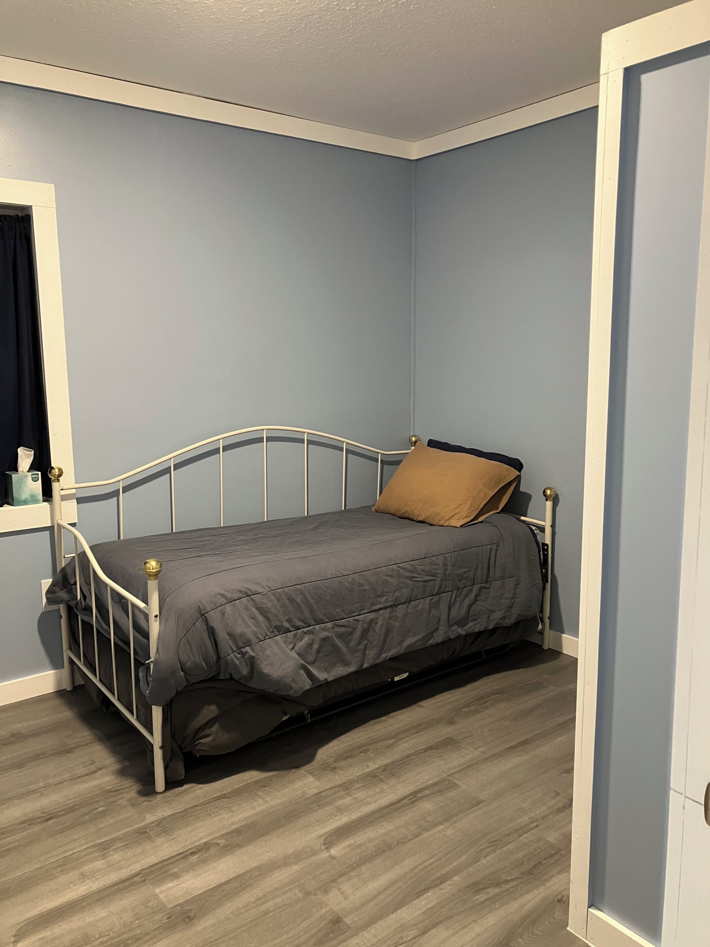 Un lit simple dans une chambre aux murs bleu clair et au plancher en bois.