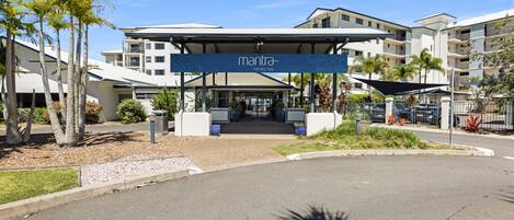 A hotel entrance with a covered walkway, palm trees, and a clear sky.