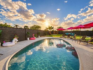 A swimming pool with lounge chairs and umbrellas, surrounded by a brick wall and greenery.