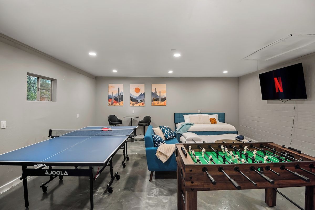 Een kamer met een tafeltennistafel, een tafelvoetbalspel, een bed, een bank en een televisie.