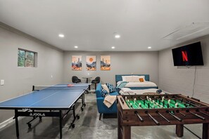 Una habitación con mesa de ping pong, mesa de fútbolín, cama, sofá y televisor.