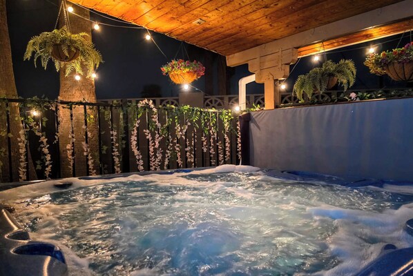 A hot tub with water jets, surrounded by a wooden deck and a fence with hanging plants.