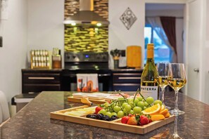 A kitchen with a countertop displaying a bottle of wine, glasses, and a fruit platter.
