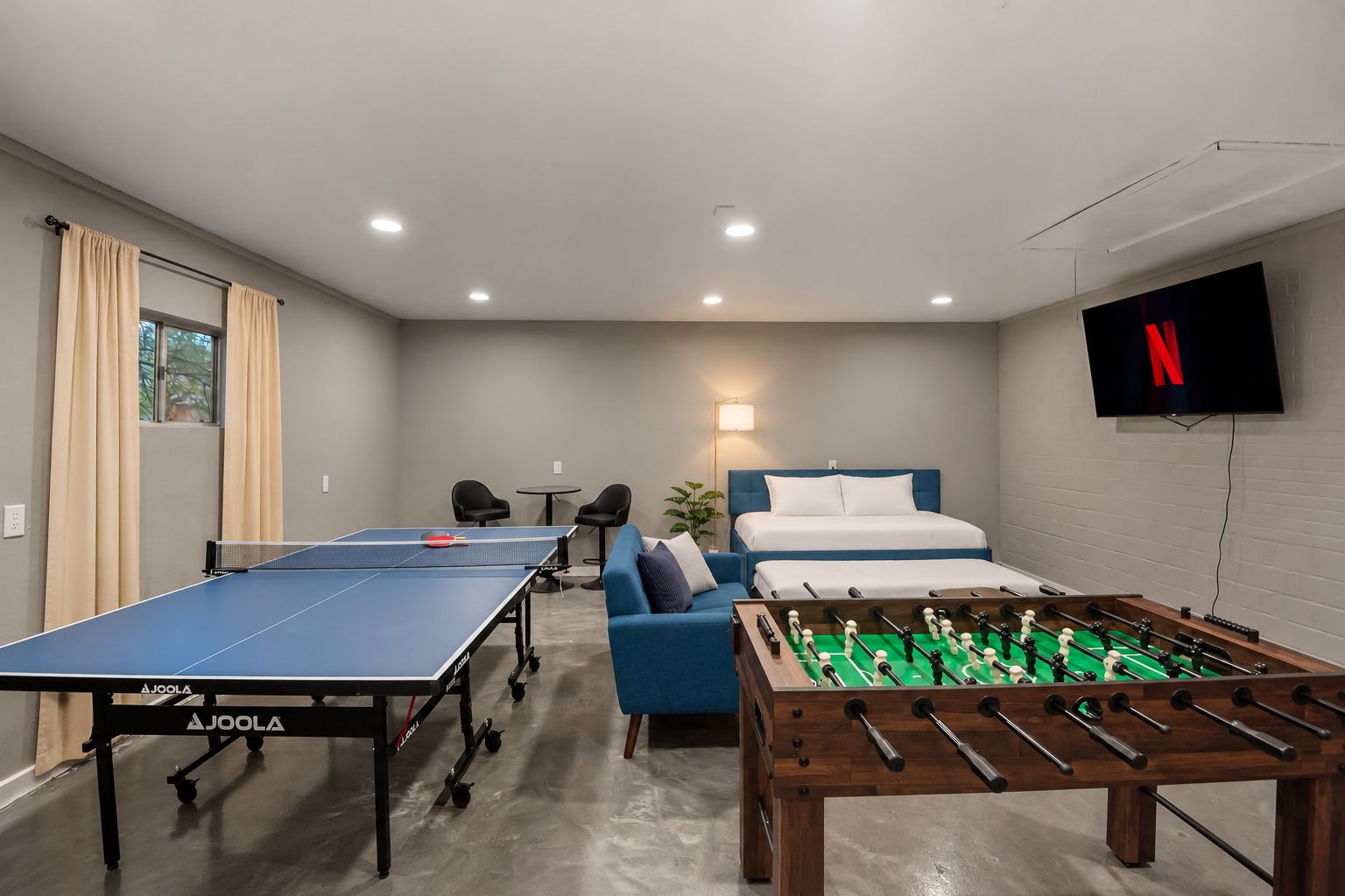 Une pièce comprenant une table de ping-pong, un baby-foot, un lit, un téléviseur et une petite table avec des chaises.