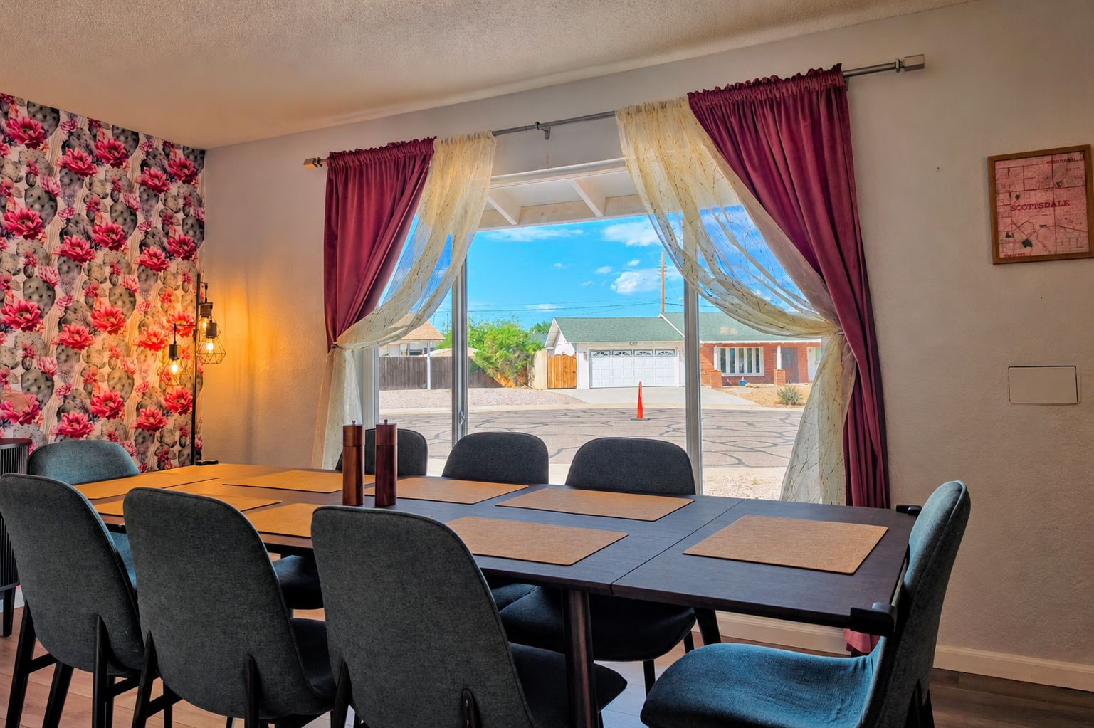 Un espace repas comprenant une table et des chaises, un mur décoré de motifs floraux et une vue sur un bâtiment à travers de grandes fenêtres.