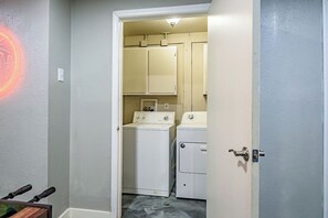 Un lavadero con lavadora y secadora, una puerta con manija, y un accesorio de luz instalado en la pared.