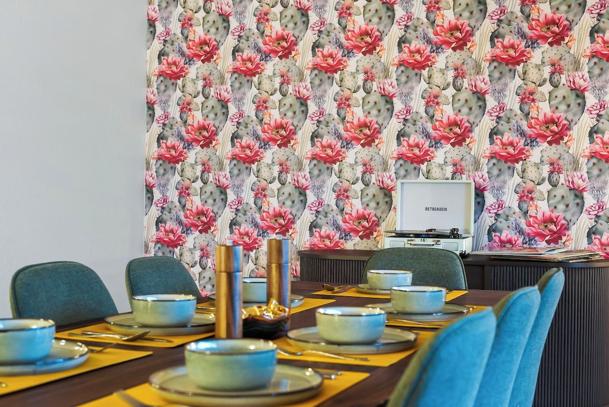 Un coin repas avec une table dressée pour quatre personnes, des chaises et un mur orné d’un motif floral.