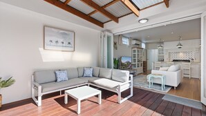 A modern living room with a sectional sofa, a coffee table, and a view into the kitchen area. - Bluestone Symmetrical Cottage With Outdoor Area (Adelaide)