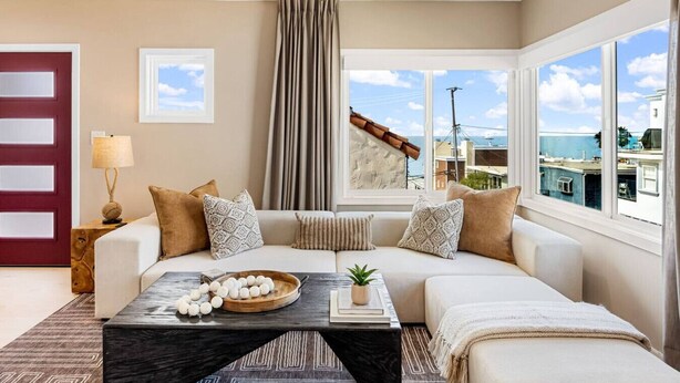 Un salón moderno con un juego de sofá, una mesa de centro con objetos decorativos y ventanas amplias con vistas a la ciudad.
