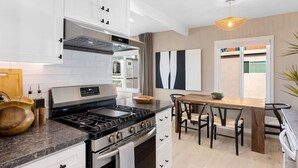 Una cocina moderna con muebles blancos, una estufa a gas y un comedor con mesa y sillas de madera.