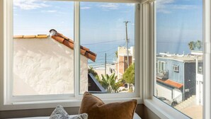 Habitación con un ventanal que da a la costa, con una pared blanca y un cojín marrón en el alféizar.