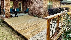 Une maison en briques avec un patio couvert, un barbecue et une terrasse en bois.