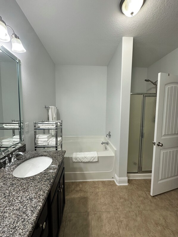 A bathroom with a granite countertop sink, a white bathtub, a glass shower enclosure, and a door leading to another room. - Stylish 3 Bedroom, 2 Bath near USA Campus-Fenced Yard + Garage (Mobile)
