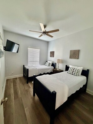 A bedroom with two beds, a ceiling fan, a TV mounted on the wall, and a window with blinds. - Stylish 3 Bedroom, 2 Bath near USA Campus-Fenced Yard + Garage (Mobile)