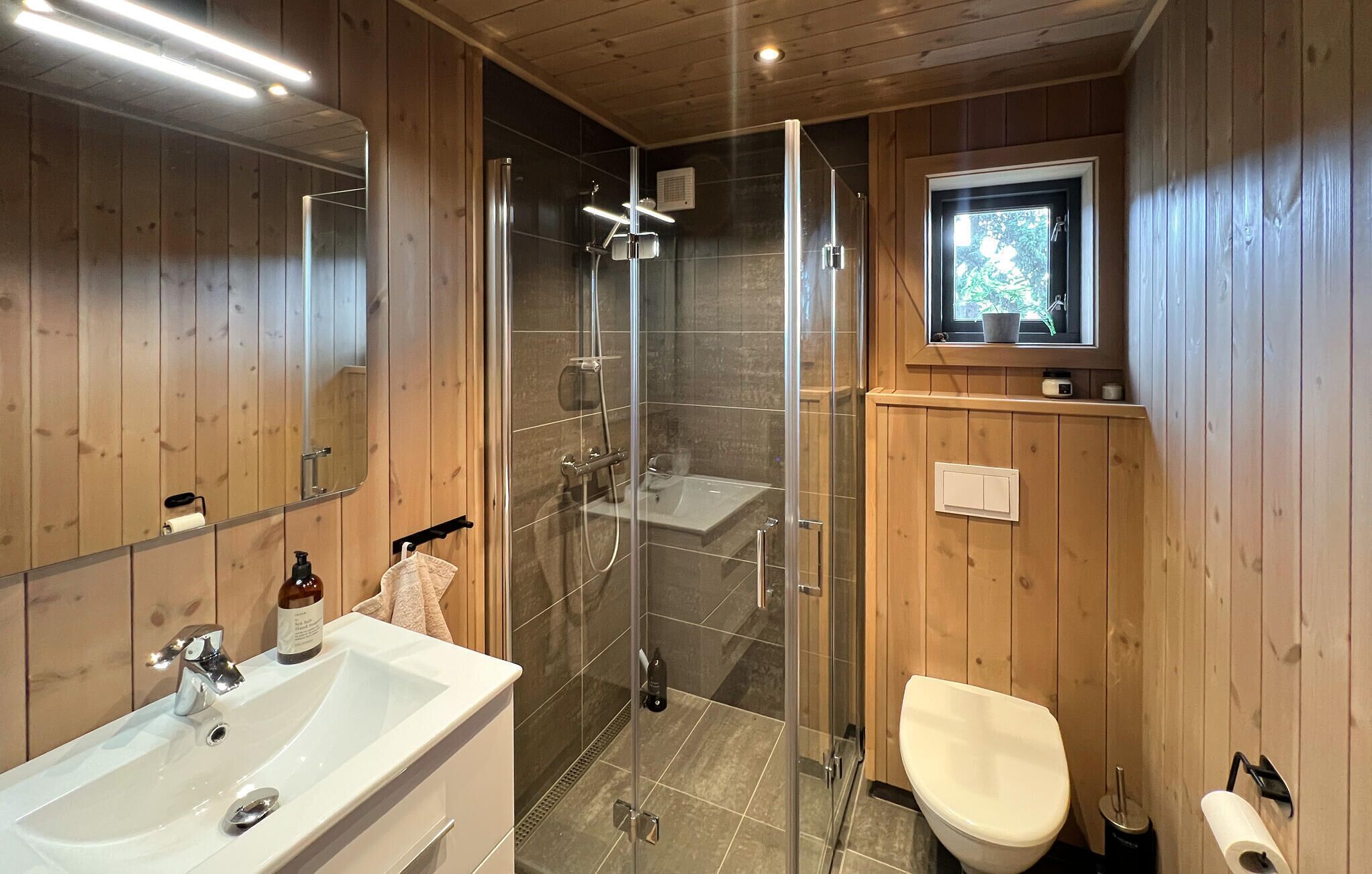 A wooden-paneled bathroom with a glass-enclosed shower, a sink, and a toilet.