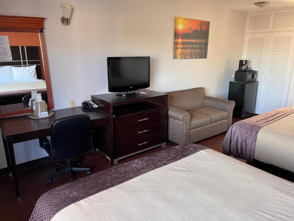 Hotellihuone, jossa on sänky, työpöytä tietokoneella, televisio ja sohva.