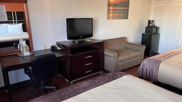 Hotellihuone, jossa on sänky, työpöytä tietokoneella, televisio ja sohva.