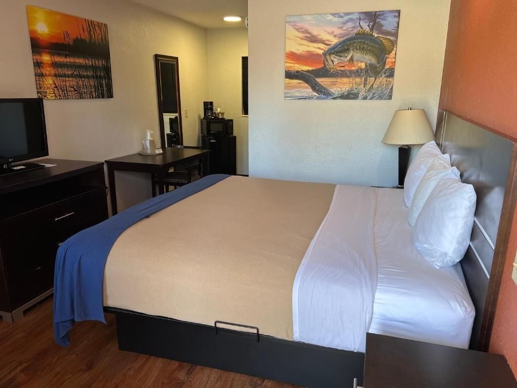Una habitació d'hotel amb un llit, un escriptori, una cadira, un televisor i obres d'art a les parets.