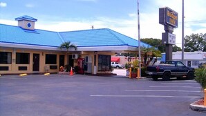 A Budget Inn with a blue roof, a Coca-Cola vending machine, and a parking lot with a black pickup truck. - Budget inn (Okeechobee)