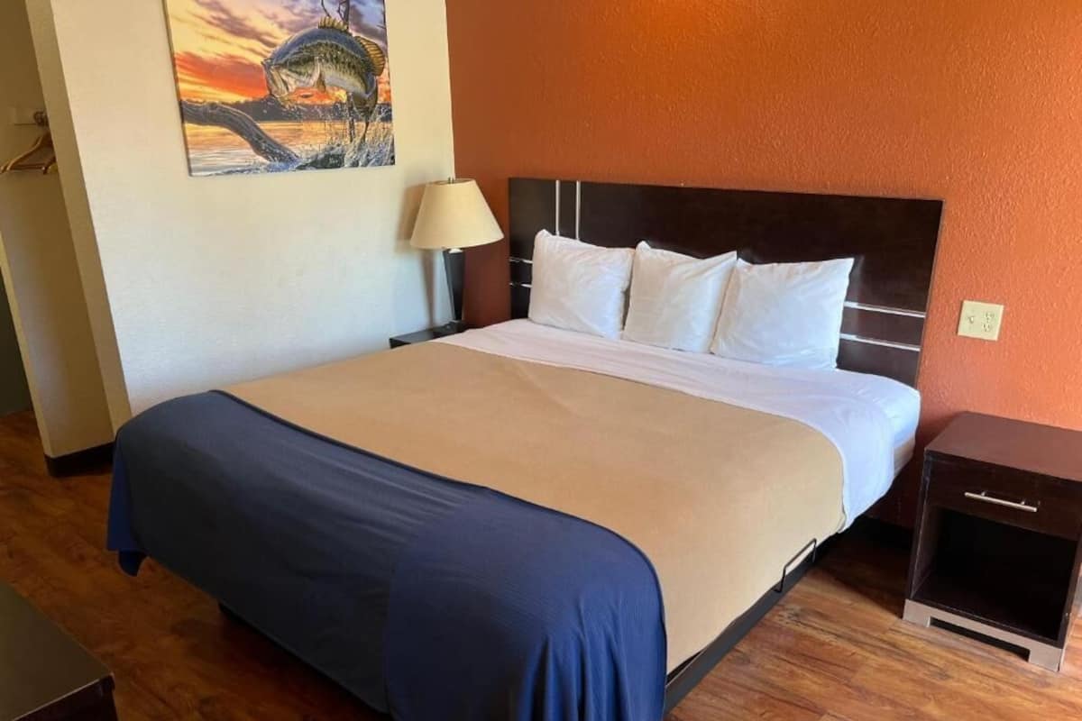 A hotel room with a bed, a nightstand, a lamp, and a painting on the wall.