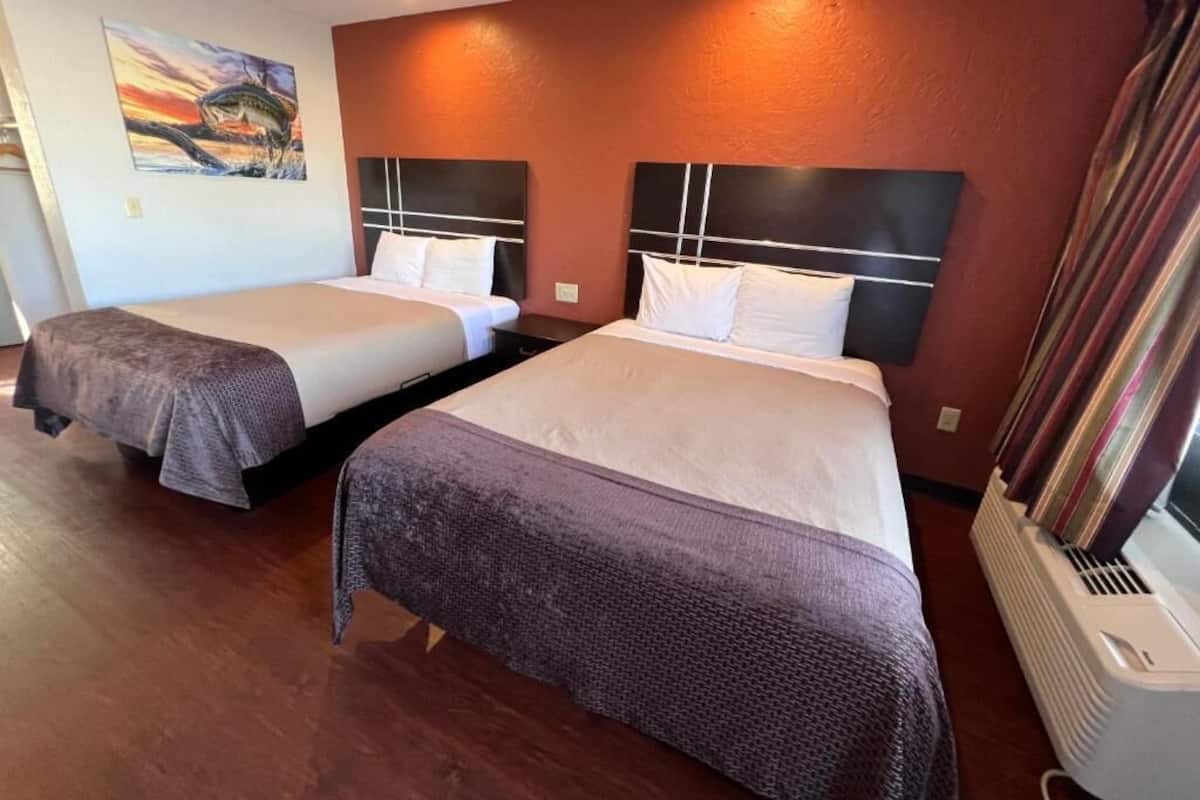 Two double beds with headboards, a painting on the wall, and a heater on the floor.