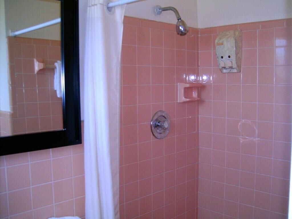A bathroom with pink tiled walls, a shower with a curtain, a mirror, and a towel rack.