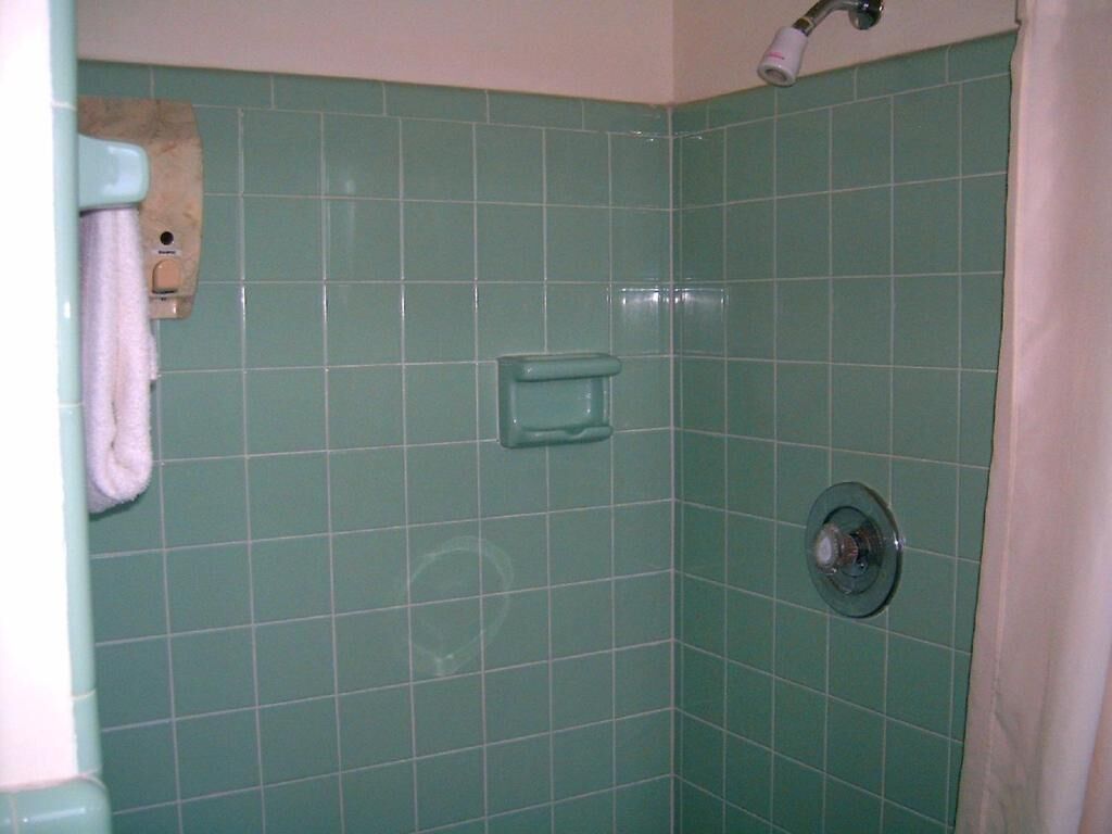 A bathroom with green tiles, a towel rack, a soap dispenser, and a shower head.