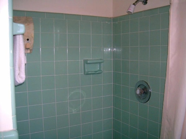 Egy fürdőszoba zöld csempékkel, törölközőtartóval, adagolóval és zuhanyfejjel.