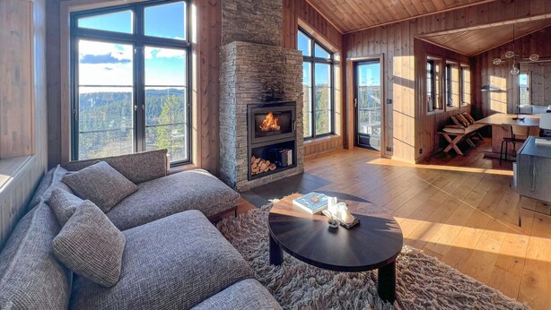 A cozy living room with a stone fireplace, large windows, a sofa, and a dining area. - Stunning home in Noresund with sauna (Noresund)