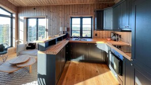 A modern kitchen with wooden cabinetry, a built-in island, and large windows offering a view of the outdoors. - Stunning home in Noresund with sauna (Noresund)