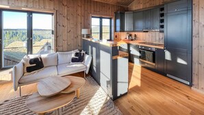 A modern kitchen with dark cabinets and a wooden countertop, a cozy seating area with a white sofa and a coffee table, and large windows offering a view of the outdoors. - Stunning home in Noresund with sauna (Noresund)