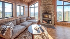 A cozy living room with a stone fireplace, large windows, and a wooden ceiling. - Stunning home in Noresund with sauna (Noresund)