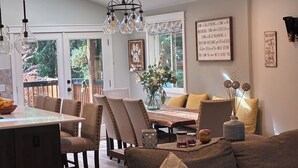 A modern kitchen with a dining area, featuring a large island, pendant lights, and a view to the outside.