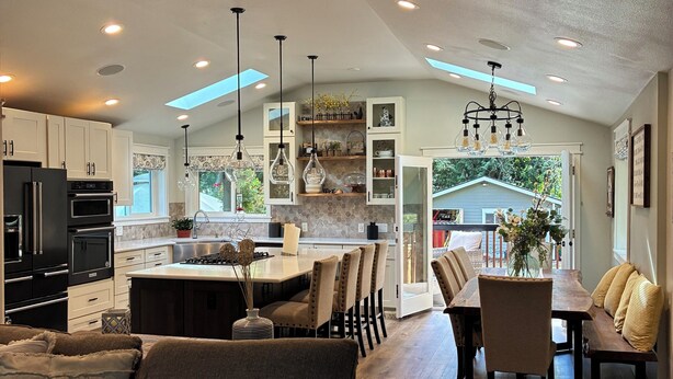A modern kitchen with white cabinets, a dining area with a wooden table and chairs, and a cozy seating area with a brown sofa.