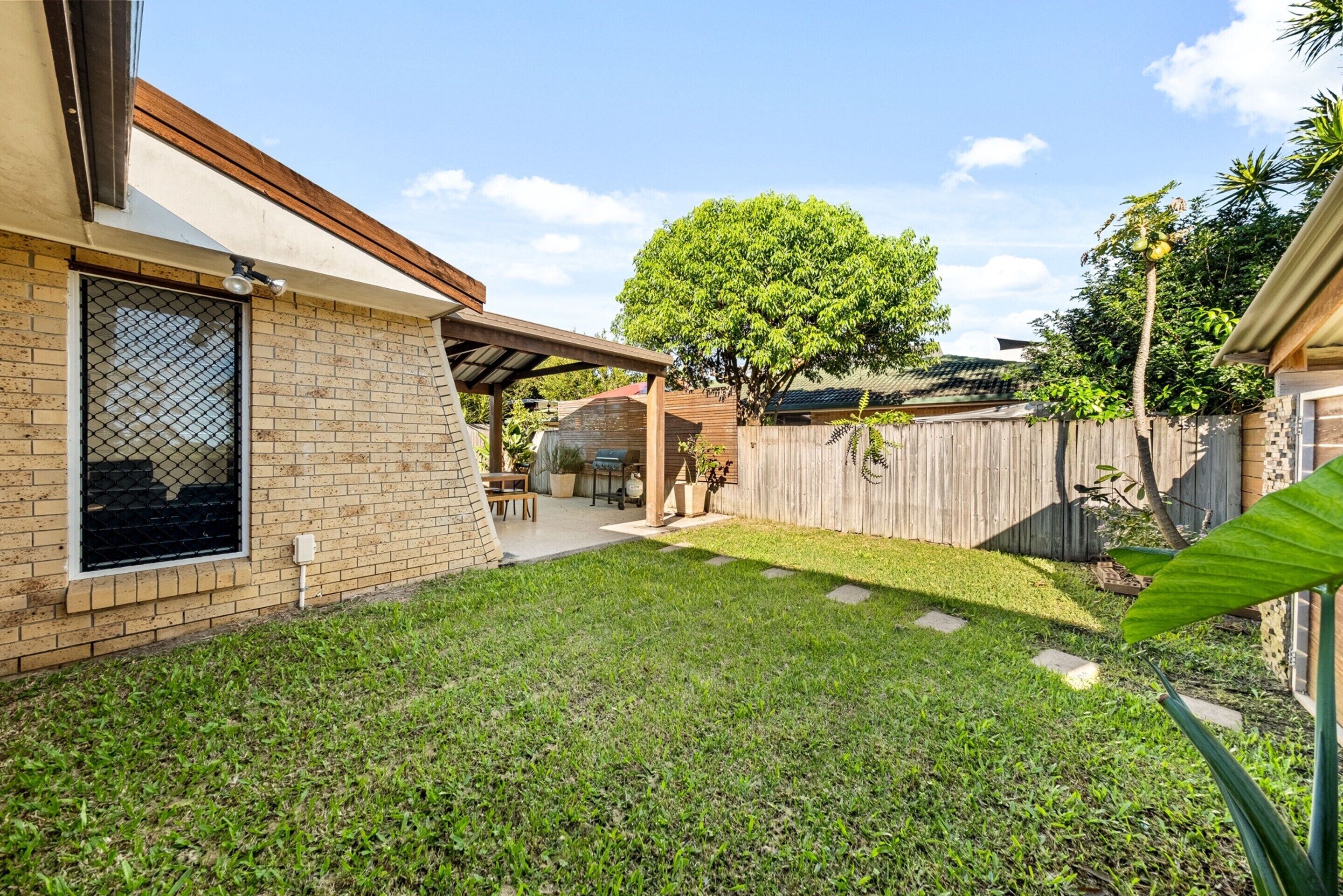 A backyard with a patio, a wooden fence, and a tree.