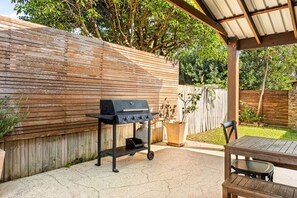 An outdoor patio with a grill, a table, and chairs.
