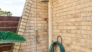 A corner shower with a hose and a water tank, a brick wall, and a wooden deck. - 2-bed Beach Escape With Courtyard (Gold Coast)