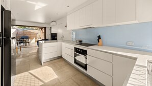 A modern kitchen with white cabinets, a black oven, and a blue backsplash. - 2-bed Beach Escape With Courtyard (Gold Coast)