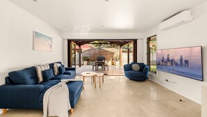 A modern living room with a sofa set, a TV, and a dining area with a table and chairs. - 2-bed Beach Escape With Courtyard (Gold Coast)