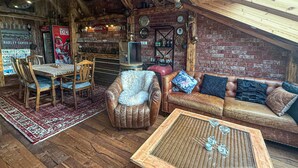 Un interior acogedor y rústico con una mesa y sillas de madera, un sofá de cuero con cojines y una mesa de centro de mimbre.