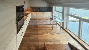 Una cocina moderna con suelo de madera, una mesa de comedor y grandes ventanales con vista a un cuerpo de agua.