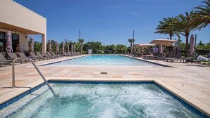 Una piscina rectangular con un jacuzzi en el centro, rodeada de sillas de descanso y sombrillas.