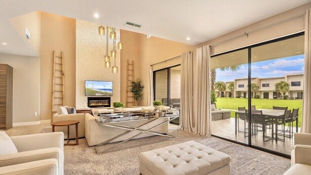 Una sala de estar moderna con un televisor de pantalla plana, asientos cómodos, una mesa de centro de vidrio y vistas a un área exterior ajardinada.