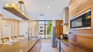 Una cocina moderna con una isla central, armarios de madera, microondas integrado y vistas al exterior.