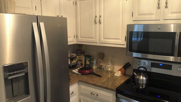 Une cuisine avec des armoires blanches, un réfrigérateur en acier inoxydable, un four à micro-ondes et une cuisinière.