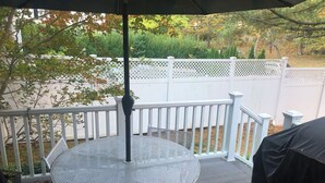 Une table ronde en métal, surmontée d’un parasol à motifs géométriques blancs, est posée sur une terrasse en bois.